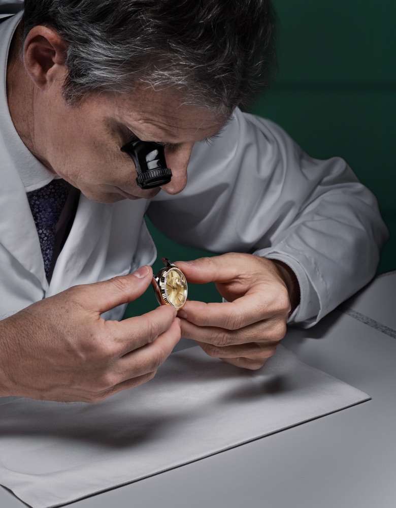 An expert watchmaker at a Rolex Authorised Service Centre inspecting a Rolex timepiece with a loupe.