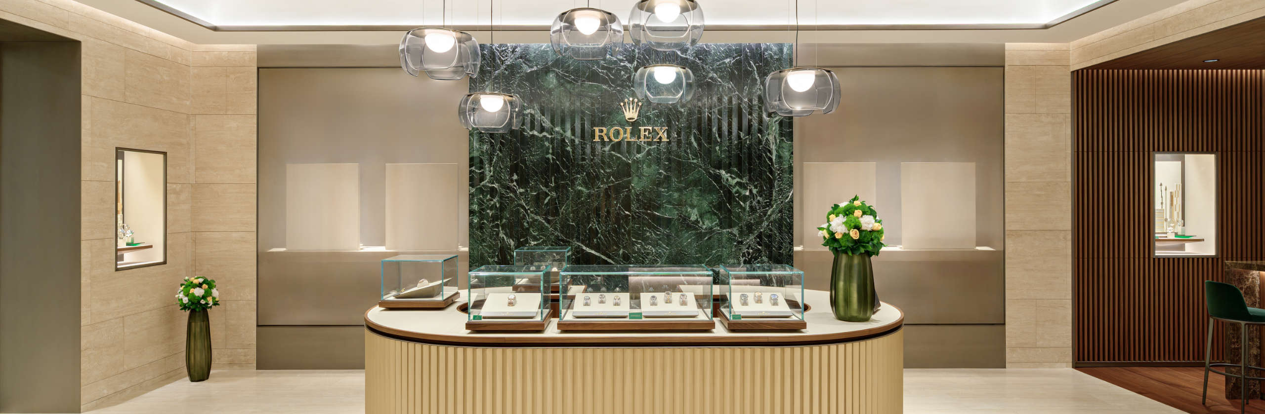 Interior of DAFC Rolex boutique with curved display counter, glass watch cases, marble back wall, and pendant lighting.