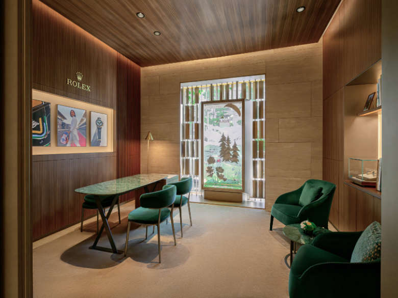 Interior of DAFC Rolex boutique in Vietnam featuring a consultation area with green velvet chairs, display case with luxury watches, and natural light from a decorative window.