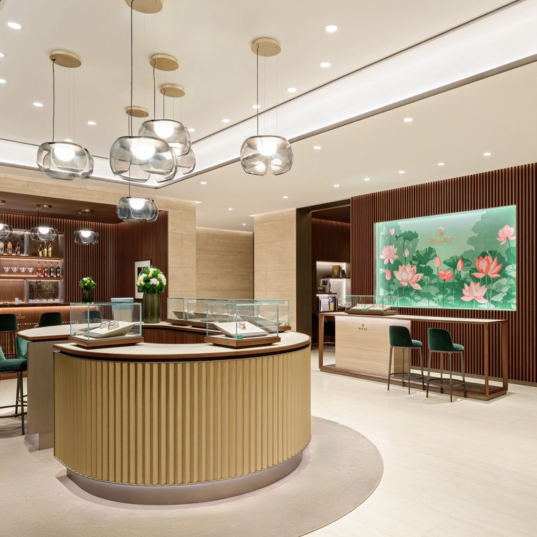 Interior of DAFC Rolex boutique in Vietnam with elegant glass display cases, wooden slatted walls, crystal pendant lights, and luxury watches showcased under warm lighting.
