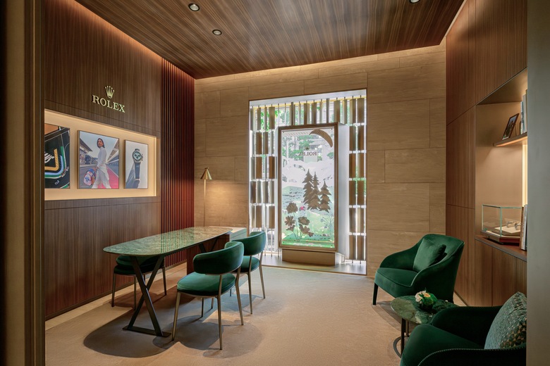 Interior of DAFC Rolex boutique in Vietnam featuring a consultation area with green velvet chairs, display case with luxury watches, and natural light from a decorative window.
